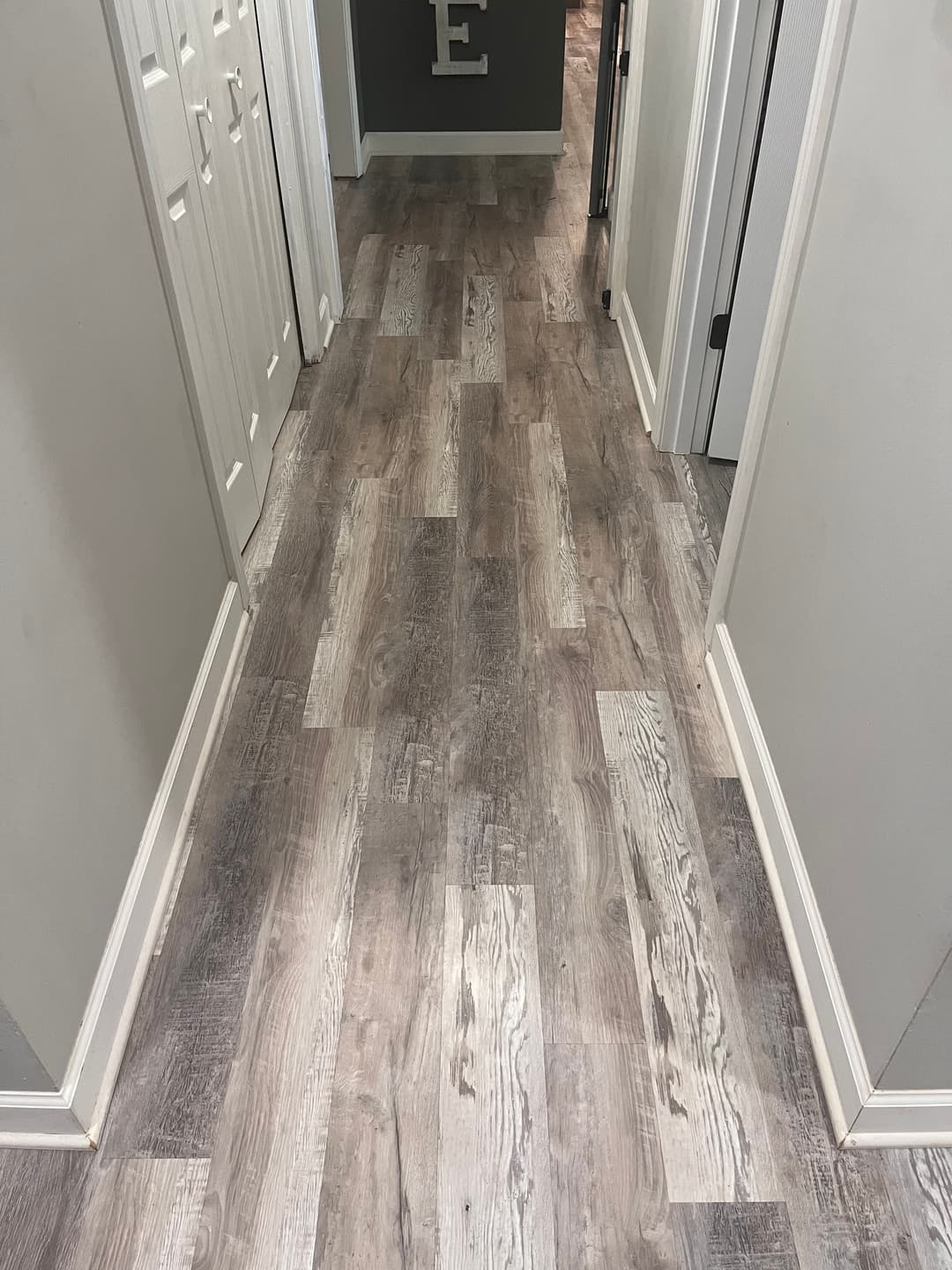 Modern gray laminate flooring in a well-lit hallway with white trim and closet doors.