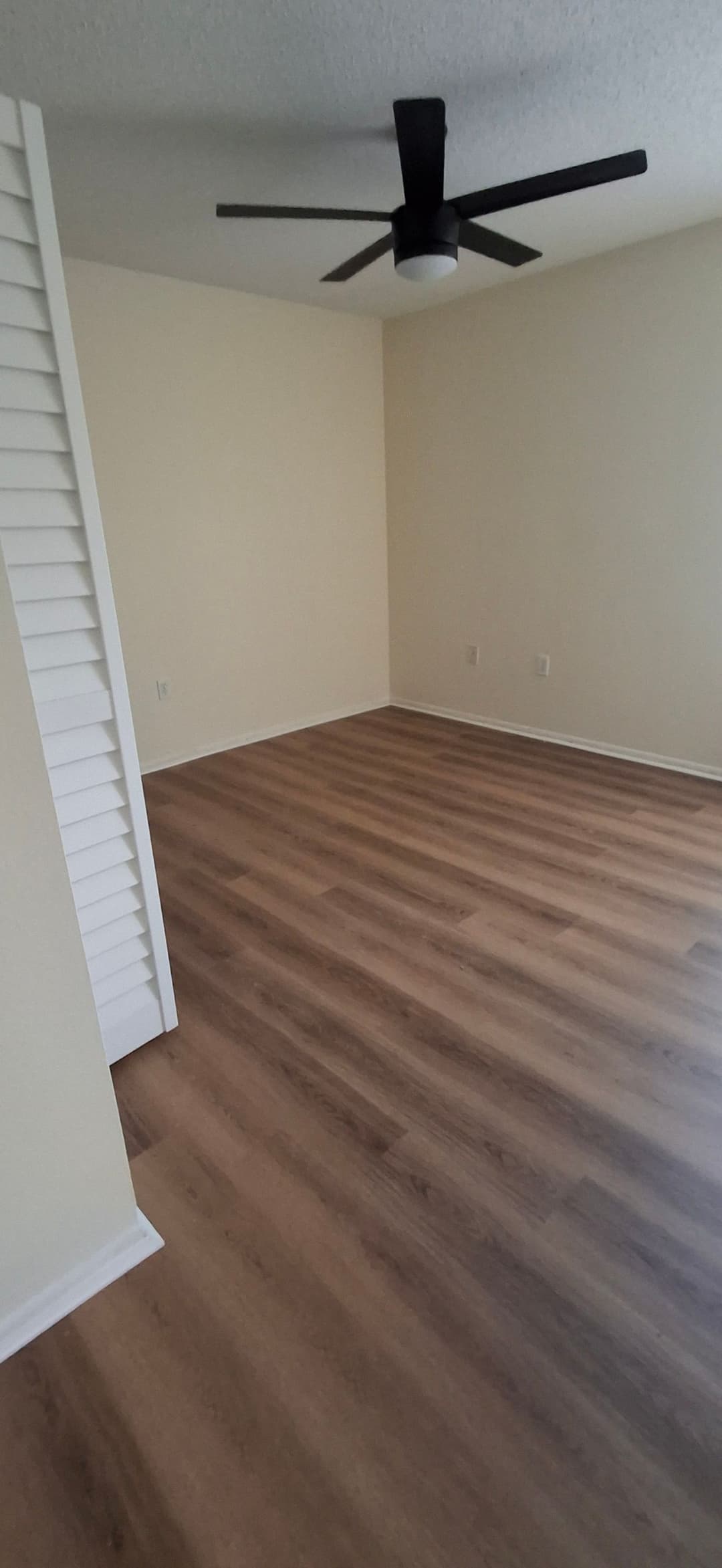 Empty room with wooden flooring, beige walls, and a ceiling fan. Ideal for living space design.