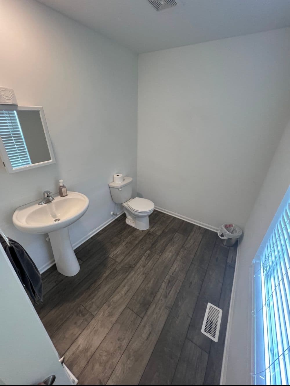 Modern bathroom featuring a sink, toilet, and wooden flooring with natural light from window.