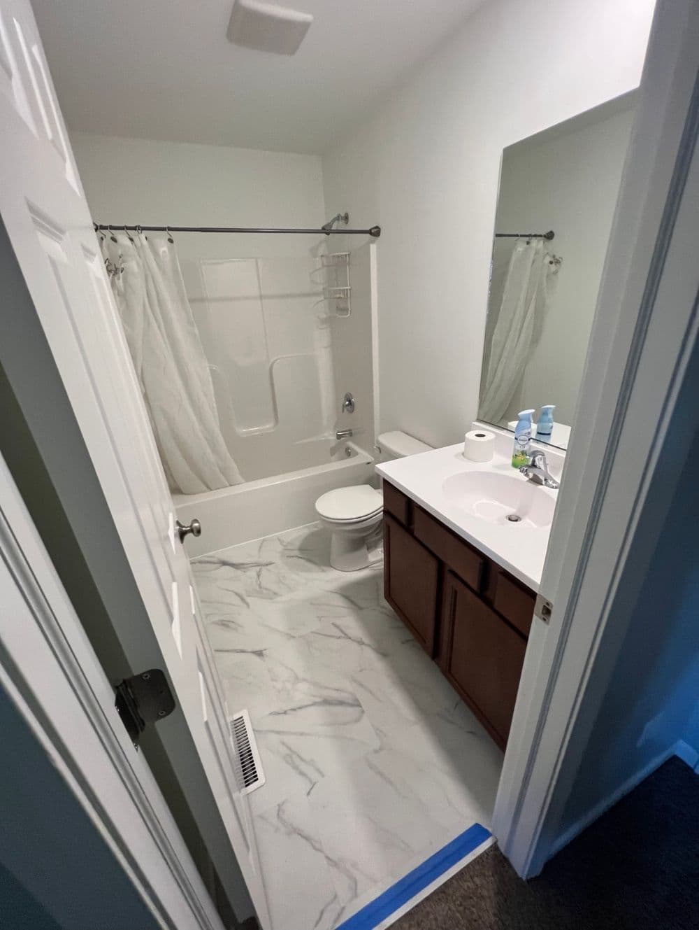 Modern bathroom with marble floor, tub, and wooden vanity, featuring white walls and natural light.