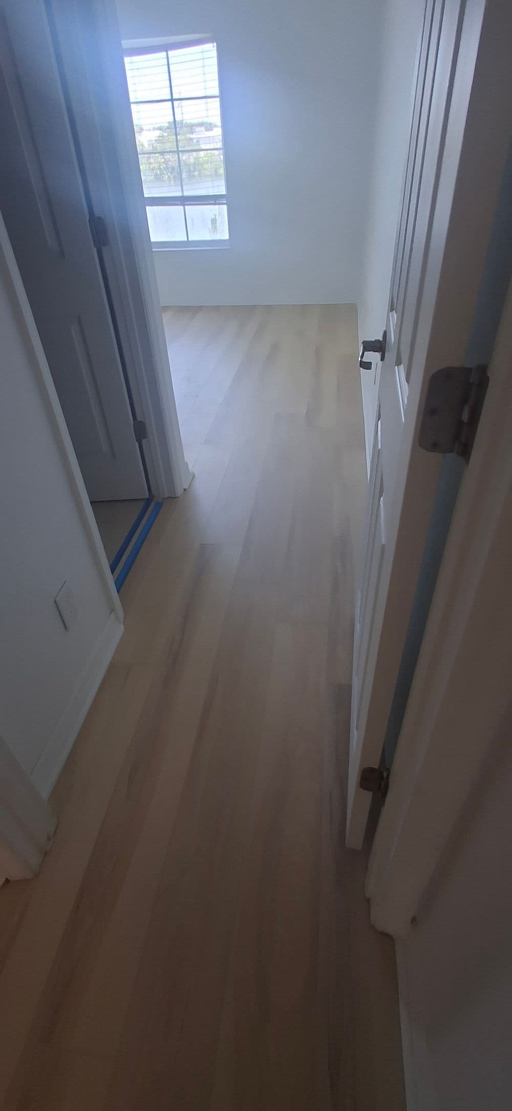 Light-filled hallway with new wooden flooring and open door to adjacent room.