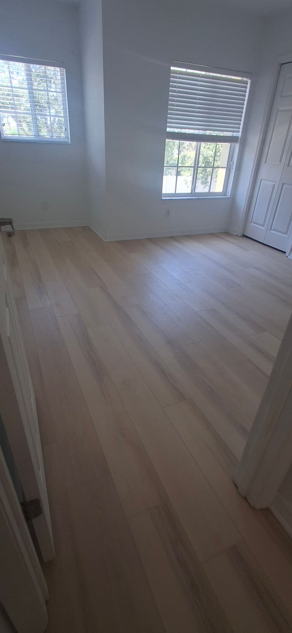 Light-filled empty room with new hardwood floors and white walls, featuring a window with blinds.