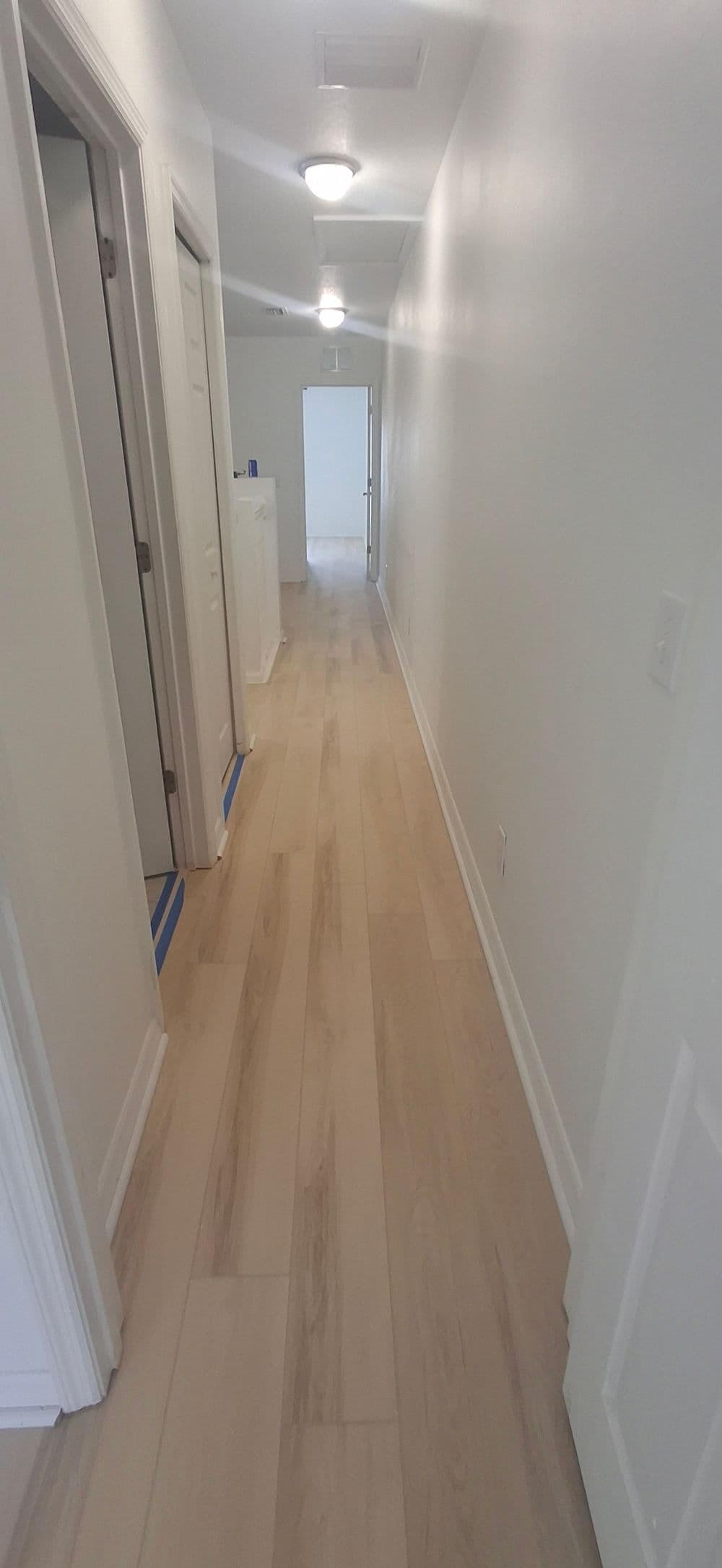 Bright and spacious hallway with light wood flooring and white walls, featuring multiple doors.