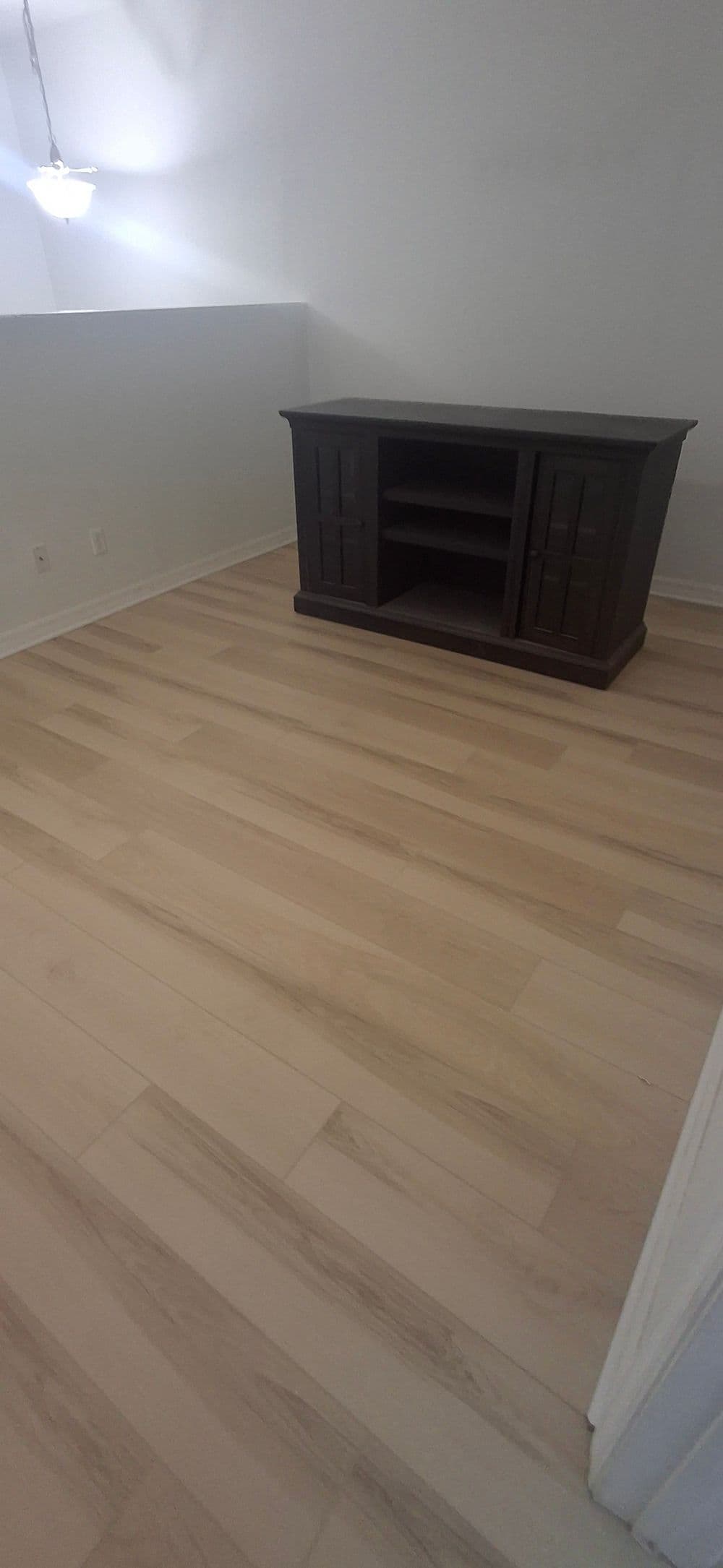 Empty room with light wood flooring and a dark wooden media cabinet against the wall.
