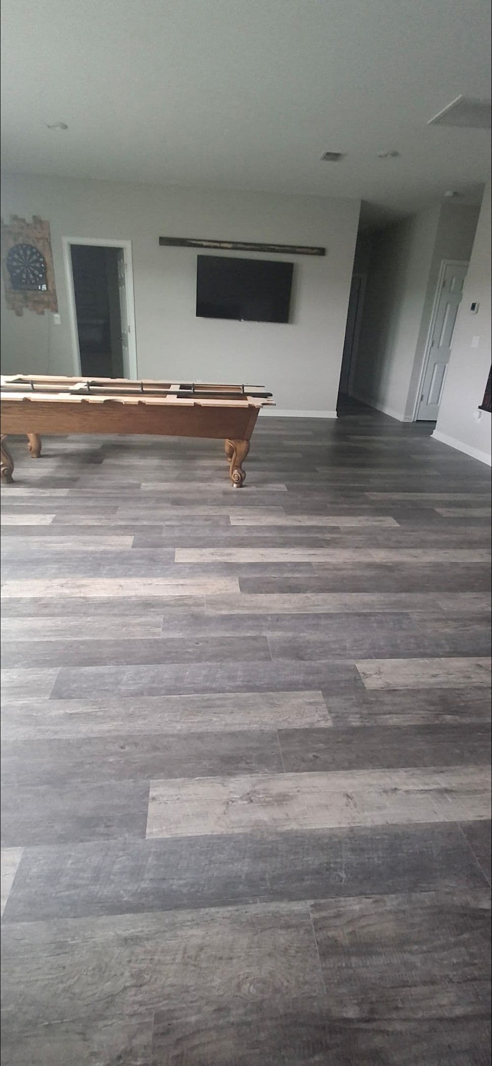 Spacious room with gray wood-like flooring, a pool table, and a TV on the wall.