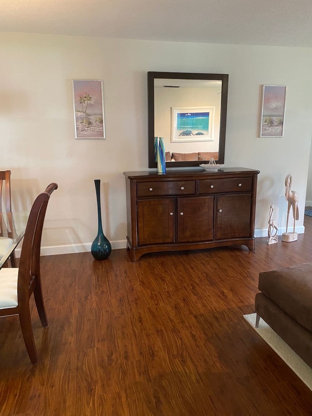 Modern living room with wooden furniture, mirror, decorative vases, and beach-themed artwork.