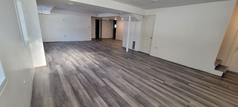 Open living space with gray laminate flooring and modern white walls, showcasing natural light.